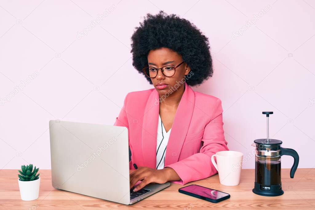 Young african american woman working at desk using computer laptop thinking attitude and sober expression looking self confident 