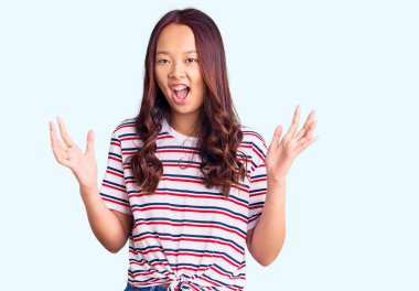 Genç, güzel Çinli kız gündelik giysiler içinde zaferi mutlu bir gülümsemeyle kutluyor ve kazanan yüz ifadesi kaldırıyor. 