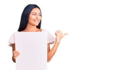 Genç, güzel, boş pankart tutan, ağzı açık gülümseyen bir Latin kız. 