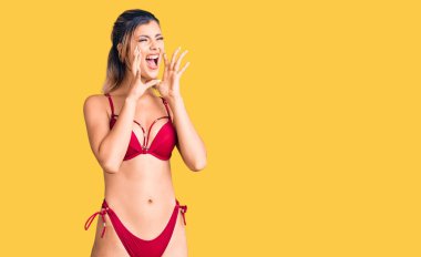 Bikini giyen genç ve güzel bir kadın elleri ağızında kızgın bir şekilde bağırıyor. 
