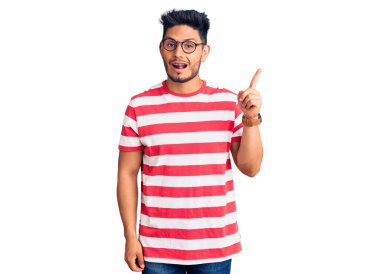 Yakışıklı Latin Amerikalı, gündelik kıyafetler giyen ve gözlüklü genç adam başarılı bir fikri işaret ediyor. Heyecanlı ve mutlu. Bir numara.. 
