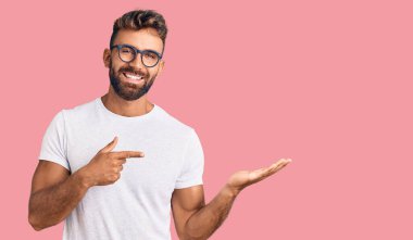 Gündelik kıyafetler giyen ve gözlüklü genç İspanyol adam kameraya hayret ediyor ve gülümsüyor.. 