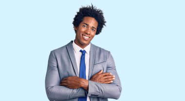 Afro saçlı, iş ceketi giyen, kollarını kavuşturup kameraya gülümseyen yakışıklı Afro-Amerikan bir adam. pozitif kişi. 