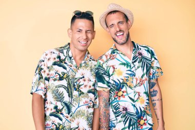 Yazlık şapkalı ve Hawaii gömlekli iki genç gay kameraya seksi bir ifadeyle bakıyor, neşeli ve mutlu bir yüzle.. 