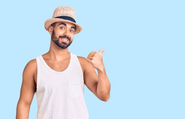 Gündelik yaz şapkası takan neşeli yüzlü genç İspanyol adam başparmağıyla yan tarafa bakıyor ve işaret ediyor.. 