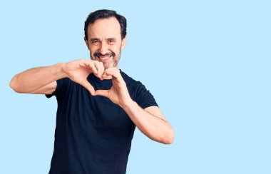 Orta yaşlı yakışıklı bir adam, gündelik tişört giyip, aşkla gülümsüyor, elleriyle kalp sembolü çiziyor. romantik kavram. 