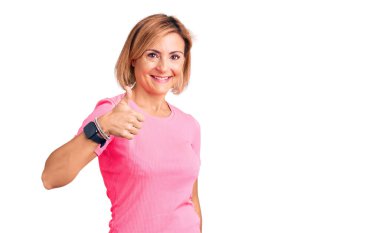 Spor giyimli genç sarışın kadın elleriyle mutlu bir jest yapıyor. Kameraya bakıp başarıyı gösteren ifade. 