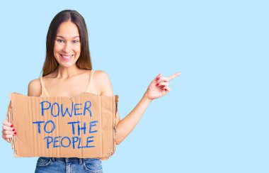 Güzel esmer, genç bir kadın gücü elinde tutuyor insanların bayrağına gülümsüyor mutlu bir şekilde el ve parmak kenarı işaret ediyor. 