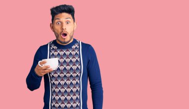 Yakışıklı Latin Amerikalı genç adam bir fincan kahve içiyor. Korkmuş ve ağzı açık kalmış, şaşırmış ve şaşırmış. 