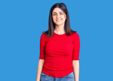 Genç ve güzel bir kız günlük tişört giyiyor. Pozitif ve mutlu görünüyor. Kendine güvenen bir gülümsemeyle ayakta duruyor ve dişlerini gösteriyor. 