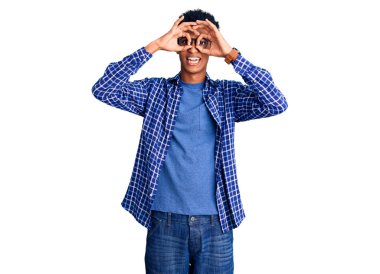 Genç Afro-Amerikan adam günlük kıyafetler ve gözlük takıyor dürbün gibi jest yapıyor, dili dışarı çıkarıyor, gözleri parmaklarından bakıyor. çılgın ifade. 