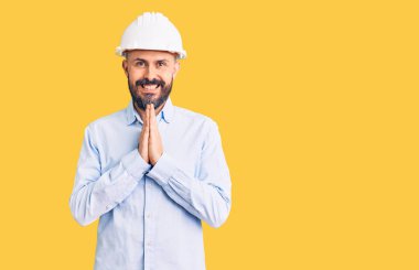 Mimar şapkası takan yakışıklı genç adam elleriyle dua ediyor af diliyor kendinden emin bir şekilde gülümsüyor.. 