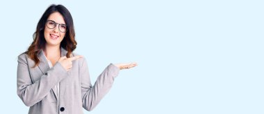 İş elbiseleri ve gözlük takan genç, güzel esmer kadın kameraya hayret ediyor ve gülümsüyor.. 