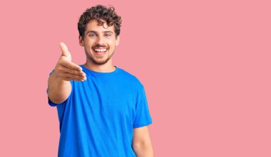 Kıvırcık saçlı, sıradan kıyafetler giyen, dostça gülümseyen ve selamlaşan genç, yakışıklı bir adam. başarılı iş. 