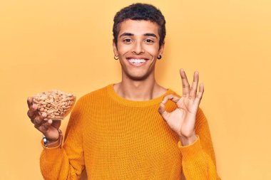 Fıstık tutan genç Afrikalı Amerikalı adam parmaklarıyla imza atıyor, gülümseyerek mükemmel bir sembol oluşturuyor. 