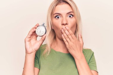 Geri sayım yapan genç, sarışın bir kadın beyaz arka plan üzerinde kronometre kullanarak ağzı elle kapatıyor, şok geçiriyor ve hata yapmaktan korkuyor. Şaşırtıcı ifade.