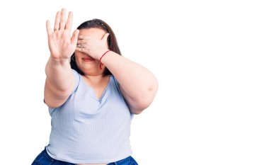 Genç ve cüsseli bir kadın, gündelik kıyafetler giyip gözleri elleriyle kapatıyor ve üzgün ve korku ifadeleriyle jestleri durduruyor. utangaç ve olumsuz kavram. 