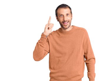 Gündelik giysiler giymiş genç yakışıklı bir adam başarılı bir fikri işaret ediyor. Heyecanlı ve mutlu. Bir numara.. 