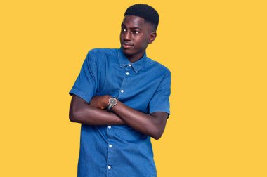 Genç Afrikalı Amerikalı sıradan kıyafetler giymiş kollarını kavuşturmuş ve kendinden emin bir şekilde yan tarafa bakıyor. 