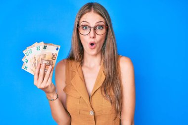 Elinde euro banknotları tutan genç sarışın kız şaşkınlık ve şaşkınlık içinde bir ifade, korku ve heyecan dolu bir yüz.. 