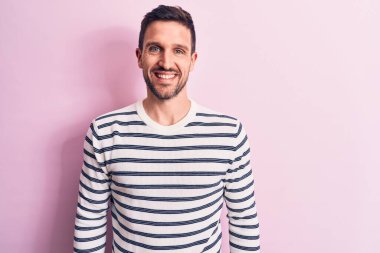 Yüzünde mutlu ve havalı bir gülümseme olan, izole pembe arka planda duran, sıradan çizgili süveter giyen genç yakışıklı bir adam. Şanslı kişi..