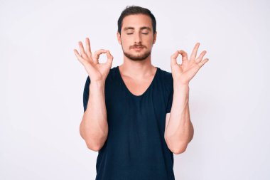 Gündelik kıyafetler giyen genç yakışıklı adam rahatla ve gözleri kapalı gülümse parmaklarıyla meditasyon hareketi yapıyor. yoga konsepti. 