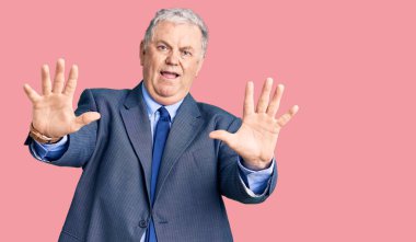 İş ceketi giyen yaşlı gri saçlı adam avuç içi hareketlerini durduruyor, kızgın ve hayal kırıklığı ifadesi takınıyor. 