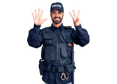 Polis üniforması giyen genç İspanyol adam sekiz numarayı gösterip işaret ederken kendinden emin ve mutlu bir şekilde gülümsüyor.. 