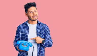 Yakışıklı Latin Amerikalı genç adam elinde antika bir telefonla gülümsüyor mutlu bir el ve parmak ile işaret ederek 