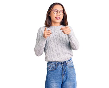 Gündelik giysiler giymiş genç, güzel Çinli kız mutlu ve komik yüzüyle kamerayı işaret ediyor. iyi enerji ve titreşimler. 