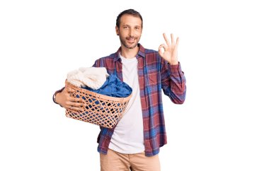 Çamaşır sepetini tutan genç yakışıklı adam parmaklarıyla imza atıyor, gülümseyerek mükemmel bir sembol oluşturuyor. 