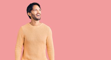 Yakışıklı İspanyol bir adam, sıradan bir süveter giyiyor. Yüzünde gülümseme, doğal bir ifade var. Kendinden emin gülen. 