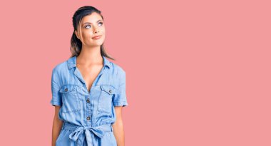 Genç, güzel bir kadın, günlük kıyafetler giymiş, gülümsüyor, yan tarafa bakıyor ve düşünüyor.. 