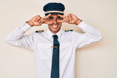 Uçak pilotu üniforması giyen genç İspanyol adam barış sembolü yapıyor. Yüzünde parmaklar, gülümseyerek zaferi gösteriyor. 