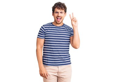 Kıvırcık saçlı, sıradan kıyafetler giyen, kameraya gülümseyen ve zafer işareti yapan genç yakışıklı bir adam. İki numara.. 