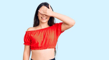 Esmer, sıradan kıyafetler giyen, gülümseyen ve gülümseyen bir genç kız, şaşırmak için gözlerini kapatıyor. kör kavram. 