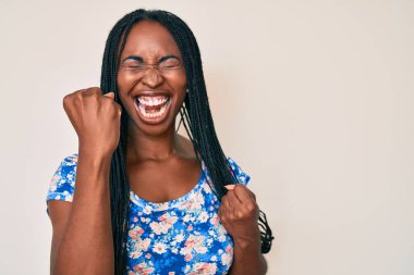 Saçları günlük kıyafetlerle örülmüş Afrika kökenli Amerikalı kadın kolları havada ve gözleri kapalı bir şekilde başarıyı kutluyor ve şaşırıyor. 