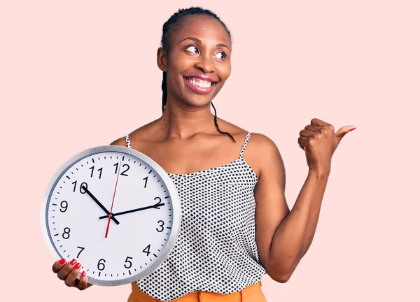 Joven Mujer Afroamericana Sosteniendo Gran Reloj Apuntando Pulgar Hacia Lado —  Fotos de Stock