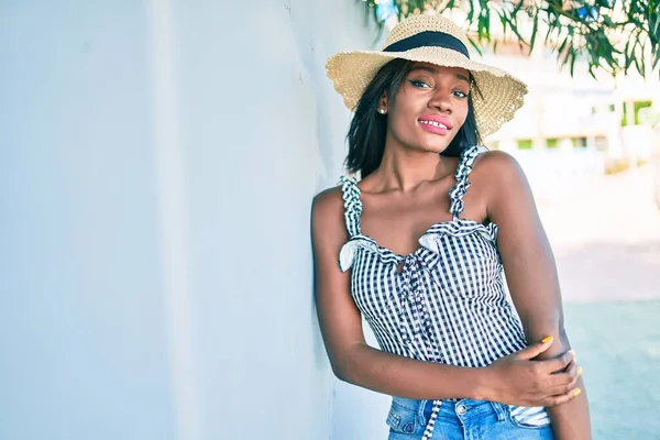Genç Afro-Amerikan kadın tatilde gülümsüyor ve şehrin duvarına yaslanıyor.