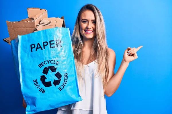 若いです美しいですブロンド女性リサイクル保持紙リサイクルバッグフルの紙の笑顔幸せなポインティングで手と指で側面 — ストック写真
