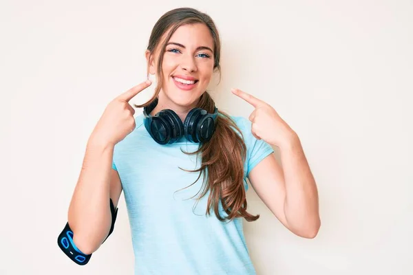 Krásná Mladá Běloška Tělocvičně Oblečení Pomocí Sluchátek Veselým Úsměvem Ukazuje — Stock fotografie