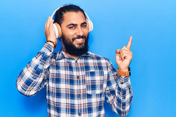 Młody Arabczyk Słuchający Muzyki Pomocą Słuchawek Uśmiechnięty Szczęśliwy Wskazując Ręką — Zdjęcie stockowe