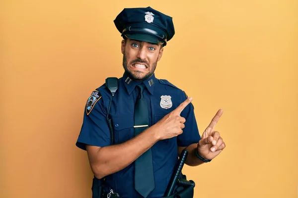 Handsome hispanic man wearing police uniform pointing aside worried and nervous with both hands, concerned and surprised expression