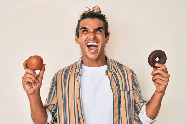 Joven Hispano Sosteniendo Manzana Roja Donut Enojado Loco Gritando Frustrado — Foto de Stock