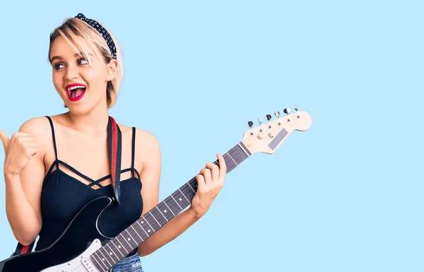 Joven Hermosa Mujer Rubia Tocando Guitarra Eléctrica Apuntando Pulgar Hacia —  Fotos de Stock