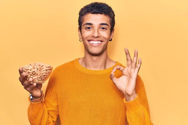 Fıstık tutan genç Afrikalı Amerikalı adam parmaklarıyla imza atıyor, gülümseyerek mükemmel bir sembol oluşturuyor. 