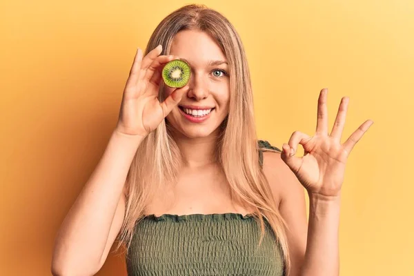 Mladá Blondýna Žena Drží Kiwi Dělá Znamení Prsty Usmívá Přátelské — Stock fotografie