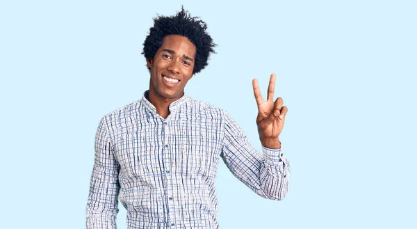 カジュアルな服を着たアフロの髪をしたハンサムなアフリカ系アメリカ人男性が 勝利のサインをするカメラで 幸せな顔をして笑っています — ストック写真