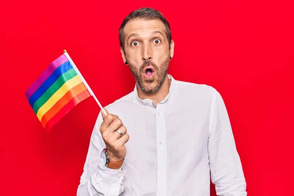 Joven Hombre Guapo Sosteniendo Arco Iris Bandera Lgbtq Asustado Sorprendido — Foto de Stock