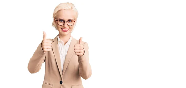 若いブロンドの女性は ビジネス服や眼鏡の成功のサインを身に着けている手で積極的なジェスチャーを行う 親指を笑顔と幸せ 陽気な表情と勝者のジェスチャー — ストック写真